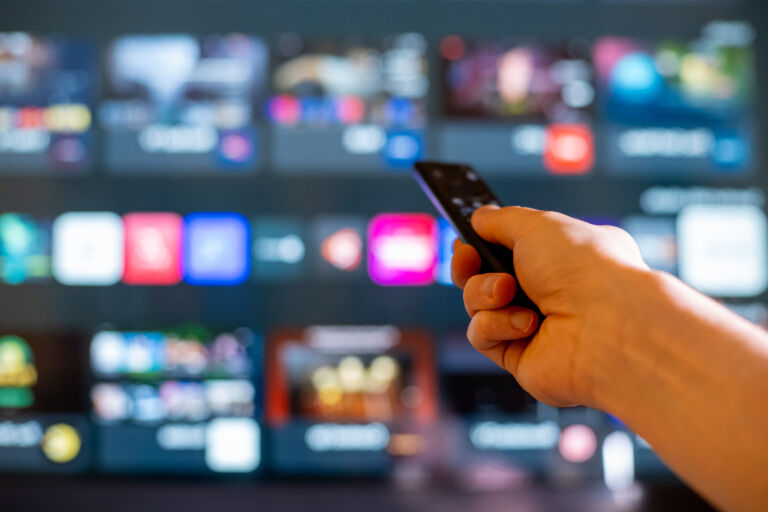 Hand Holding TV Remote Toward Blurred Smart TV Streaming